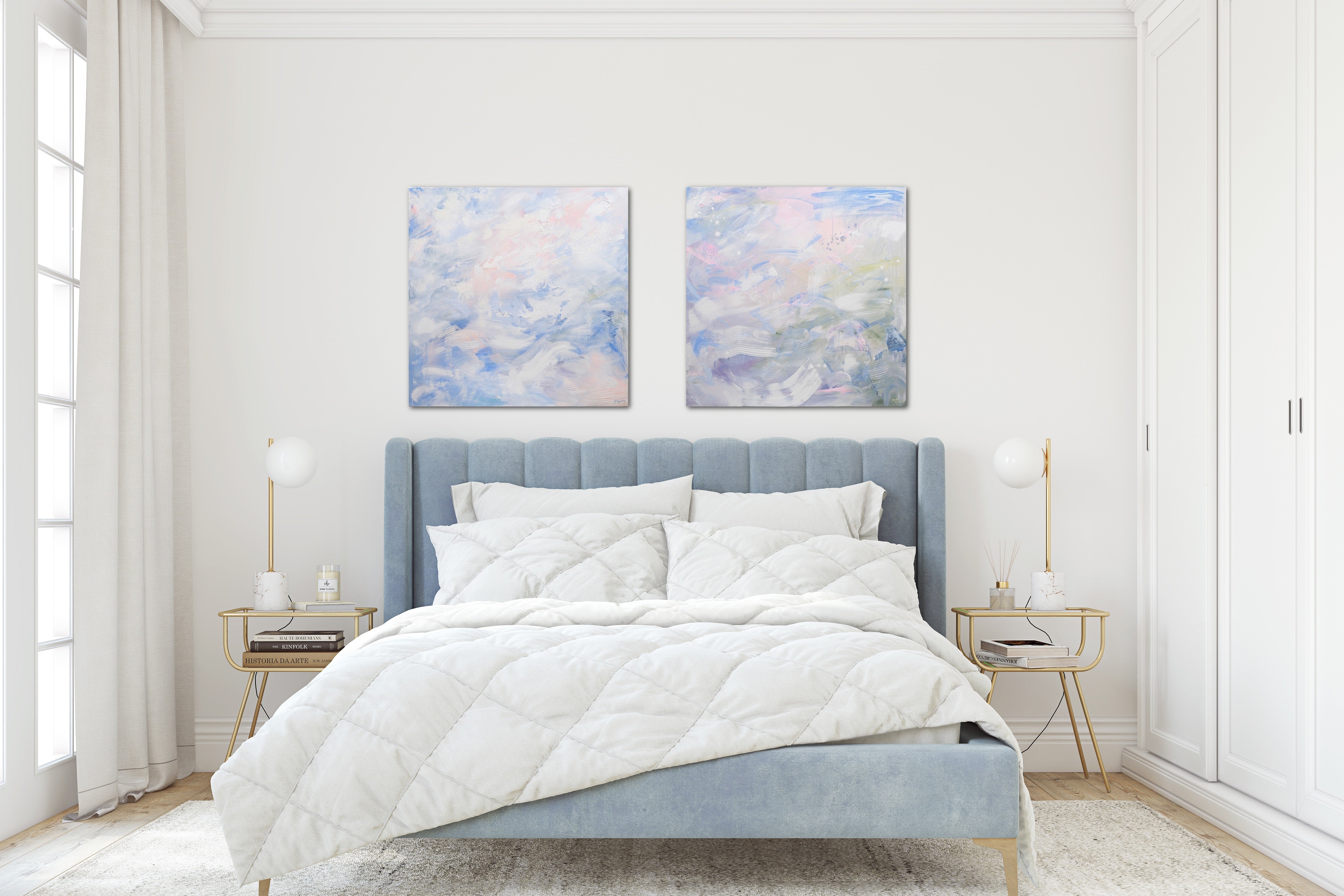 A pair of pastel toned abstract paintings hang above a tufted blue bed, flanked by gold and glass nightstands in a white and airy bedroom. 