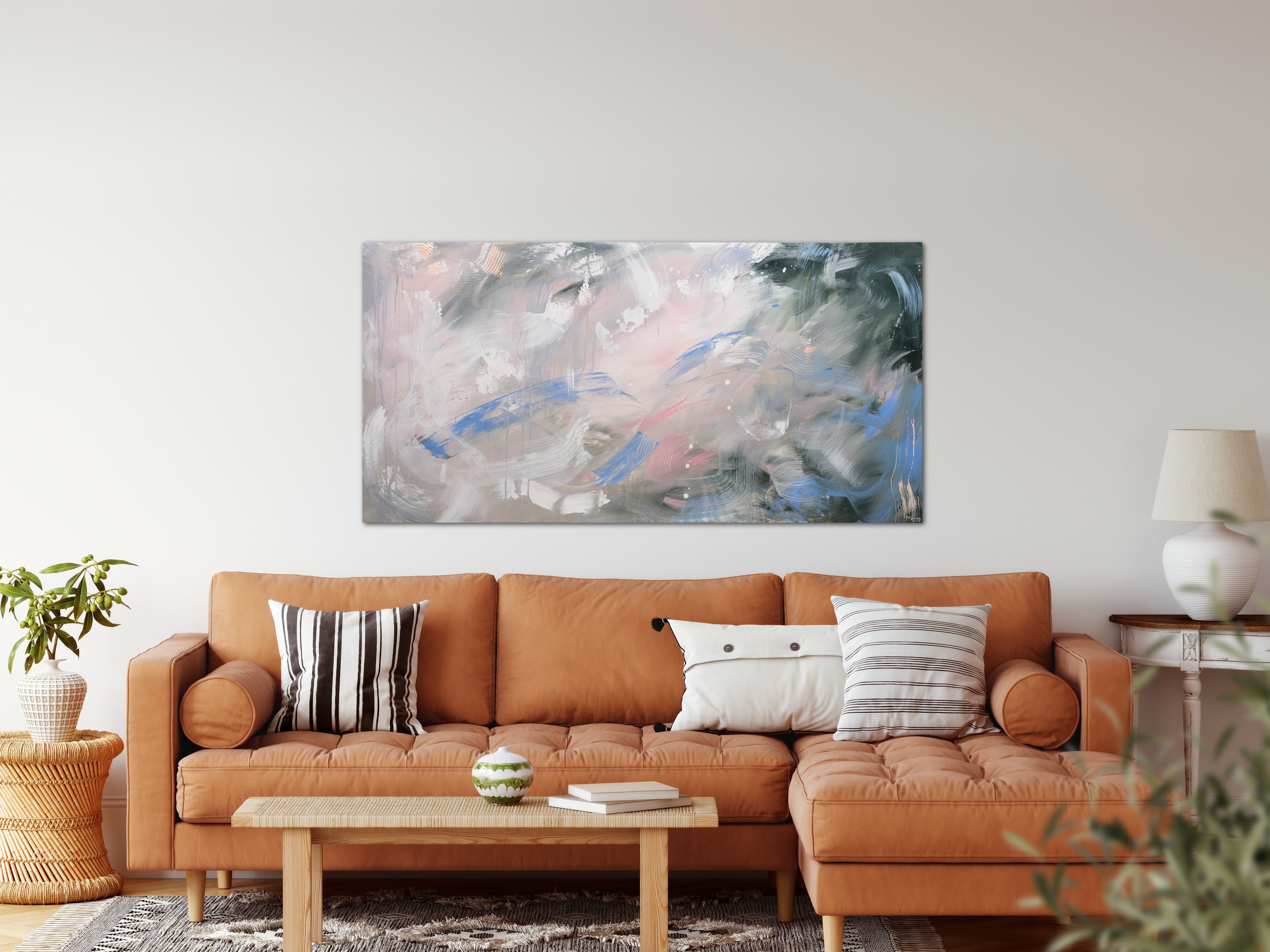 In a mid century living room, a modern green and pink painting hangs above a camel coloured leather sectional. 